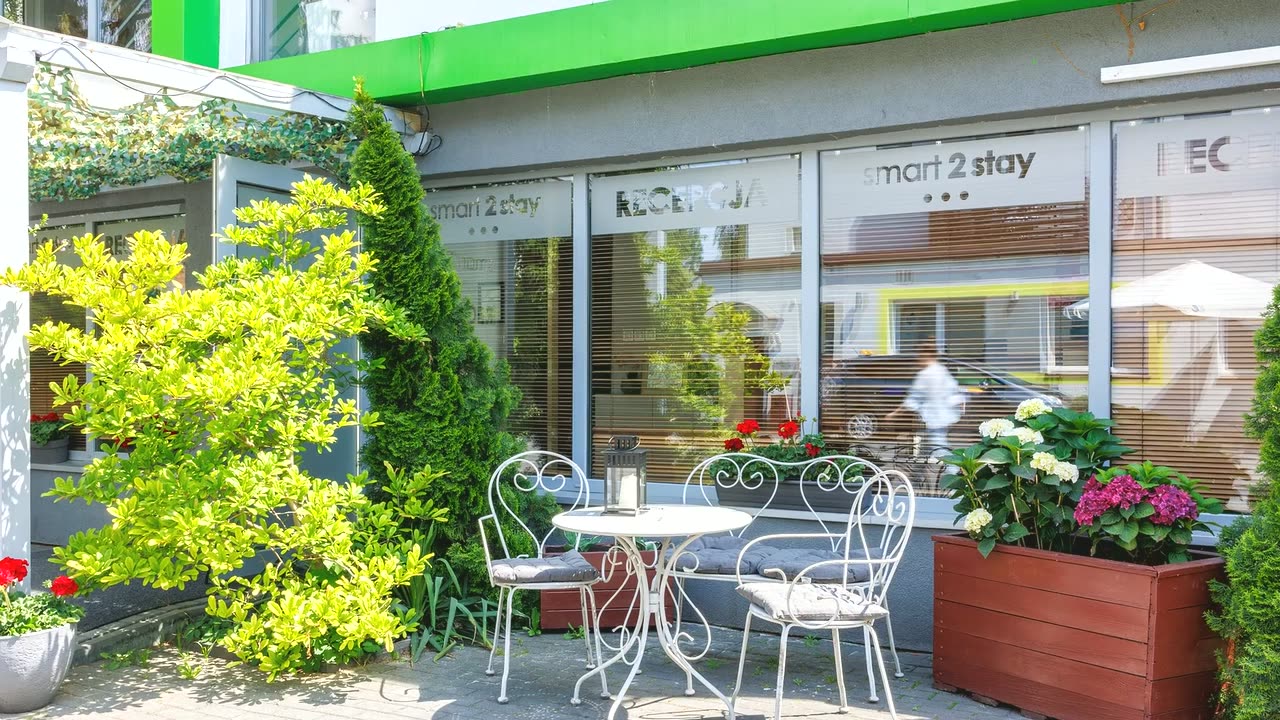Elewacja Smart2Stay Magnolia z zielonym pasem i napisem Recepcja, biały stolik z krzesłami i hortensje przed wejściem